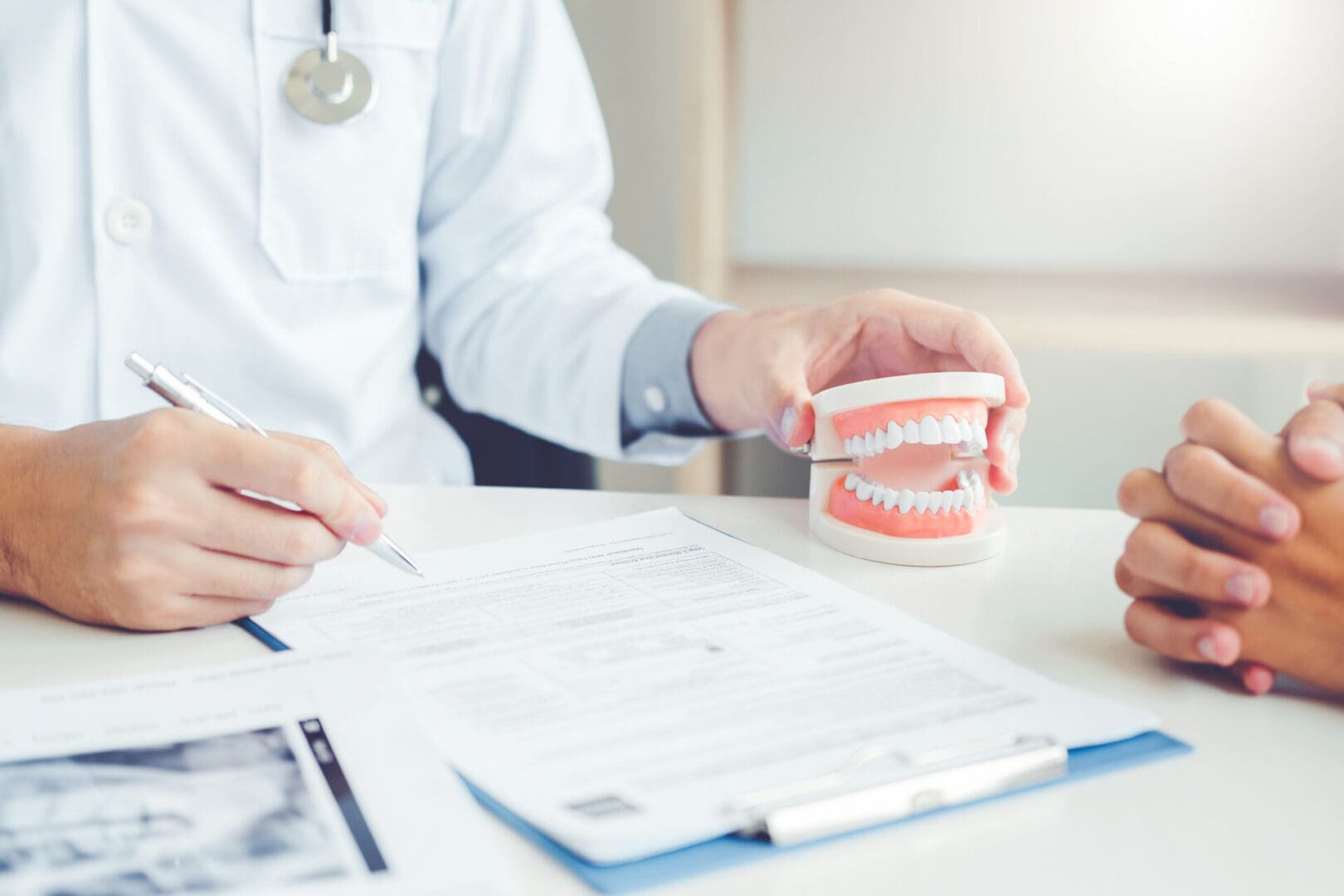 Dentist talking to smiling male patient and showing denture in dental office