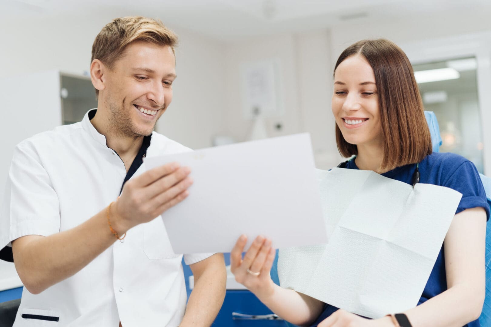 Male Professional Dentist With Gloves And Mask Holding papers photo And Show What The Treatment Will Look Like Of The Patient's Teeth. Discussion Of The Treatment Plan And Healthy Smile